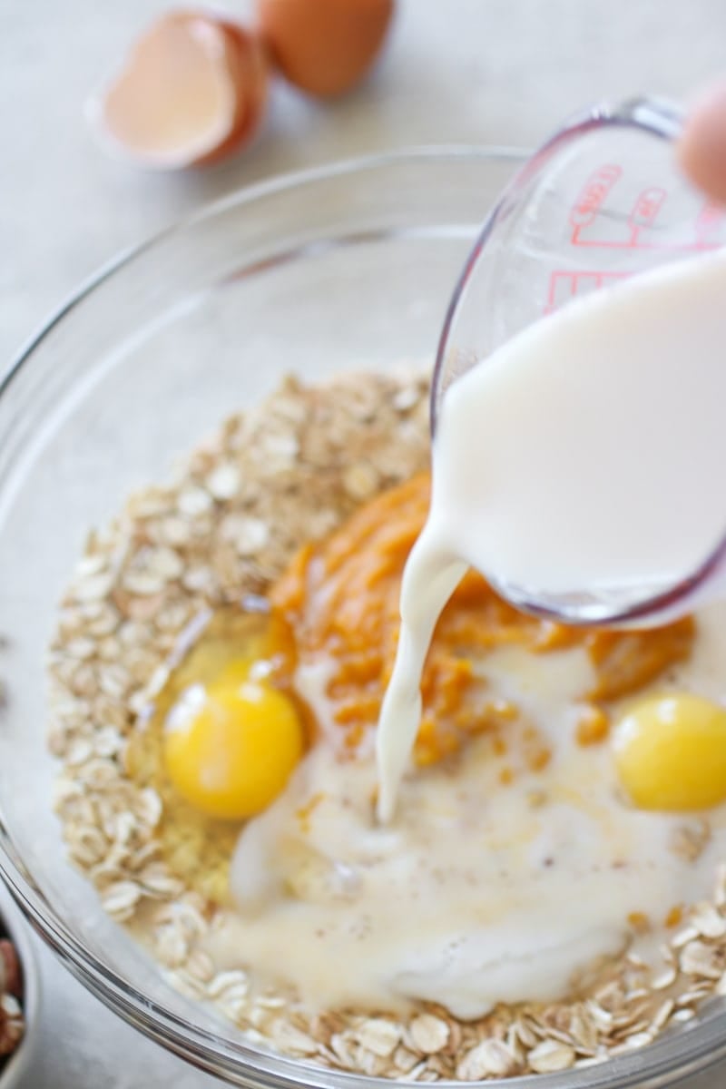 Milk being poured into a clear bowl that's holding the rest of the ingredients for the Pumpkin Baked Oatmeal.
