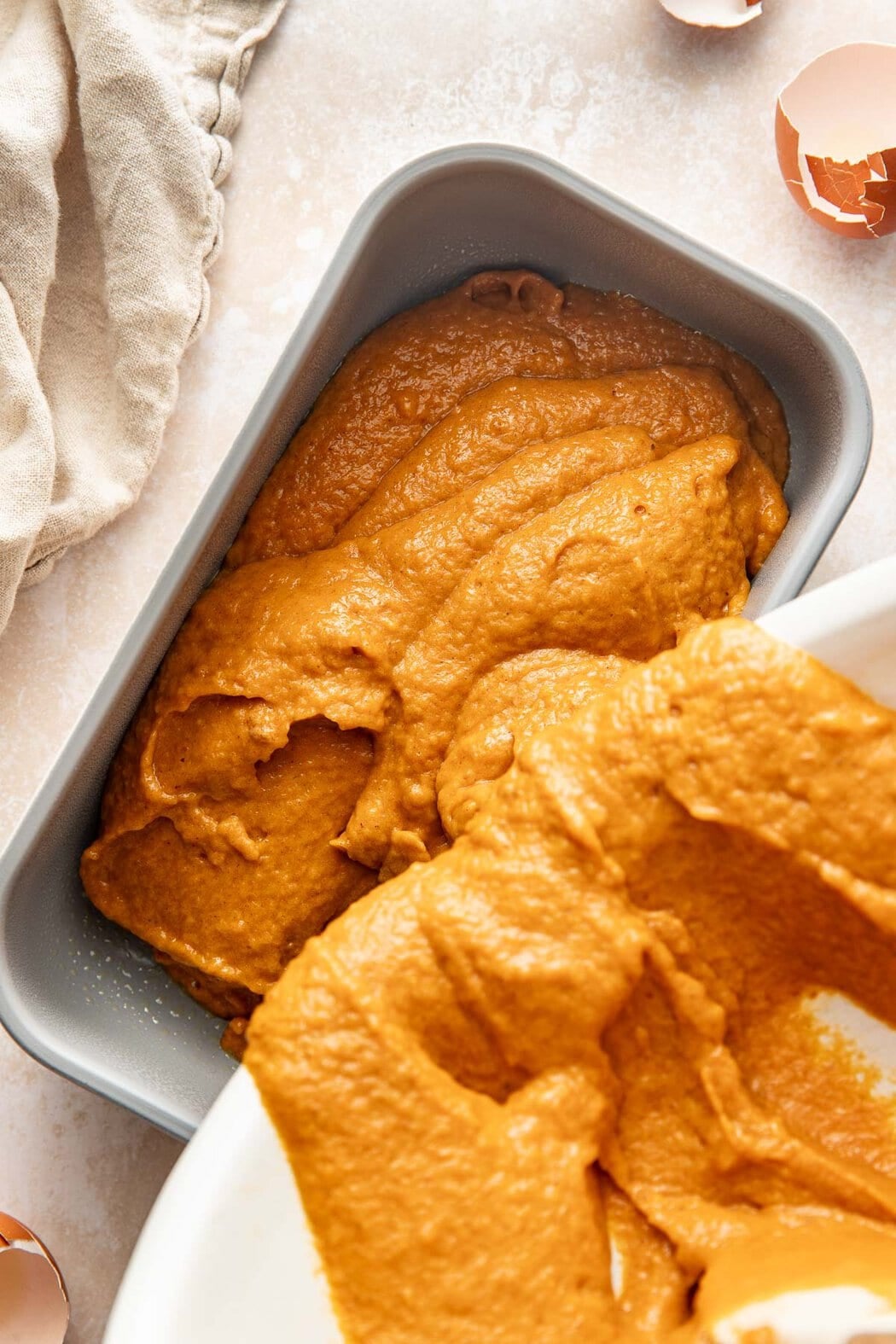 Pumpkin bread batter being poured into a loaf pan.