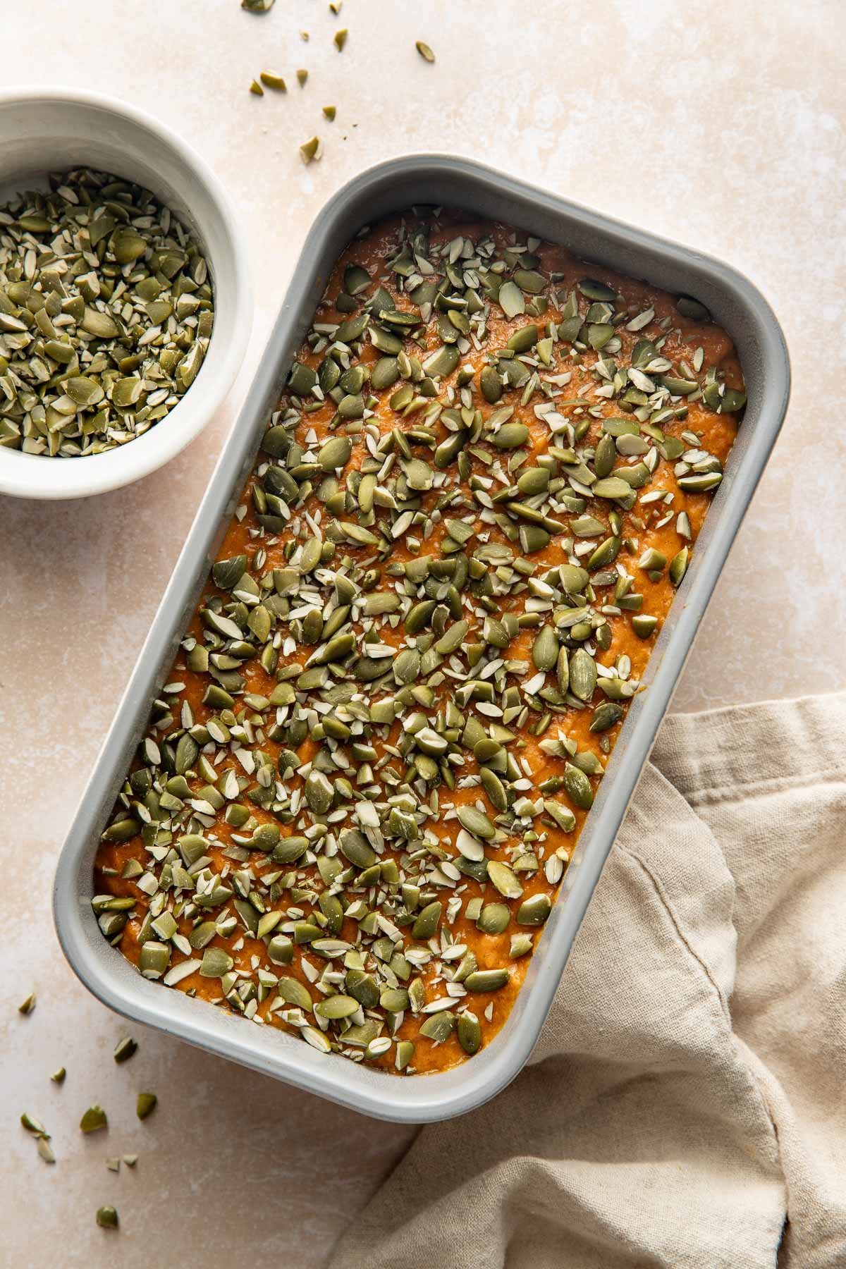 Uncooked pumpkin bread in a loaf pan topped with raw pepitas.