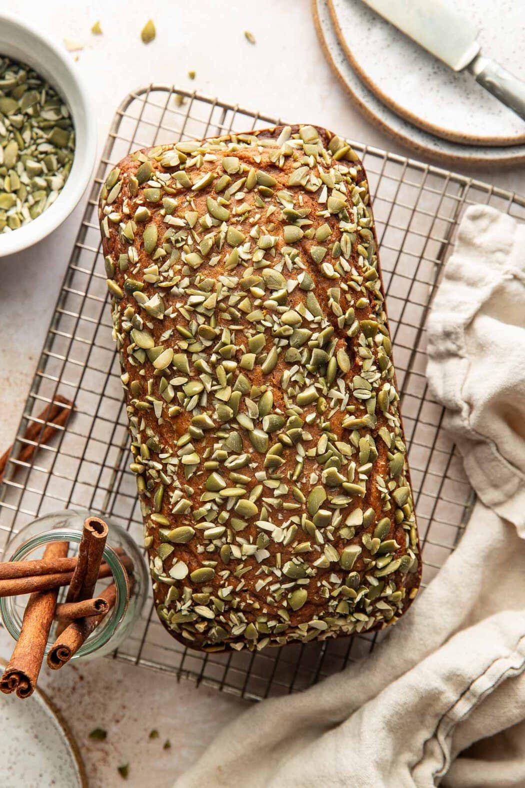 A loaf of pumpkin bread topped with crushed pepitas on a wire rack.