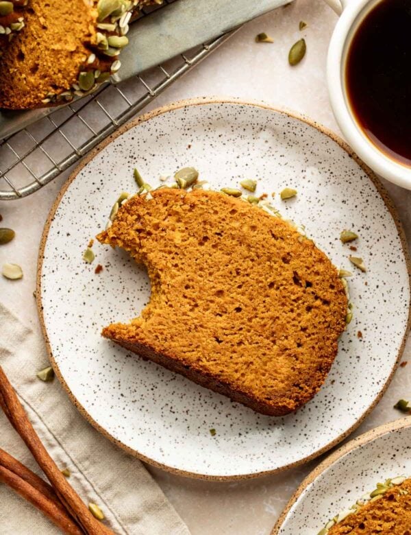A slice of pumpkin bread with a bite taken from one corner on a plate