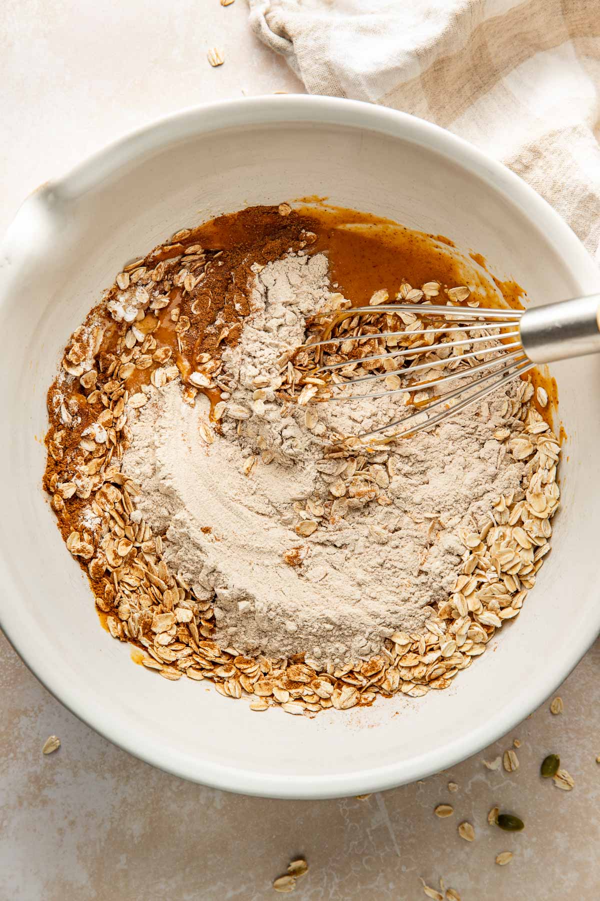 A whisk mixing wet and dry ingredients for pumpkin breakfast cookies in a bowl.