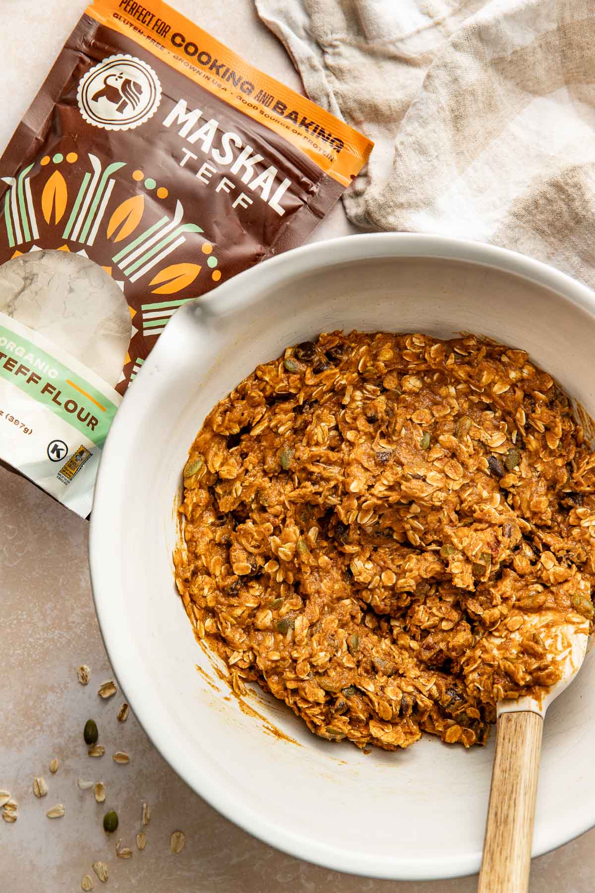 A bowl of pumpkin breakfast cookie batter next to a bag of teff flour.