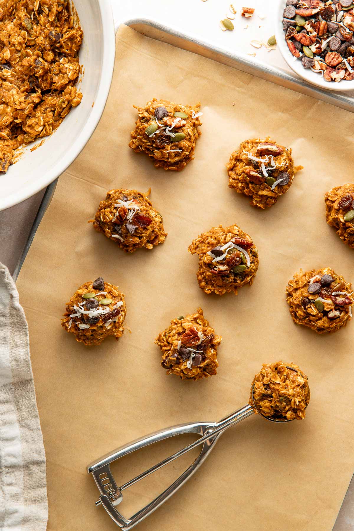 Pumpkin breakfast cookies being portioned onto a parchment lined baking sheet with a cookie scoop.