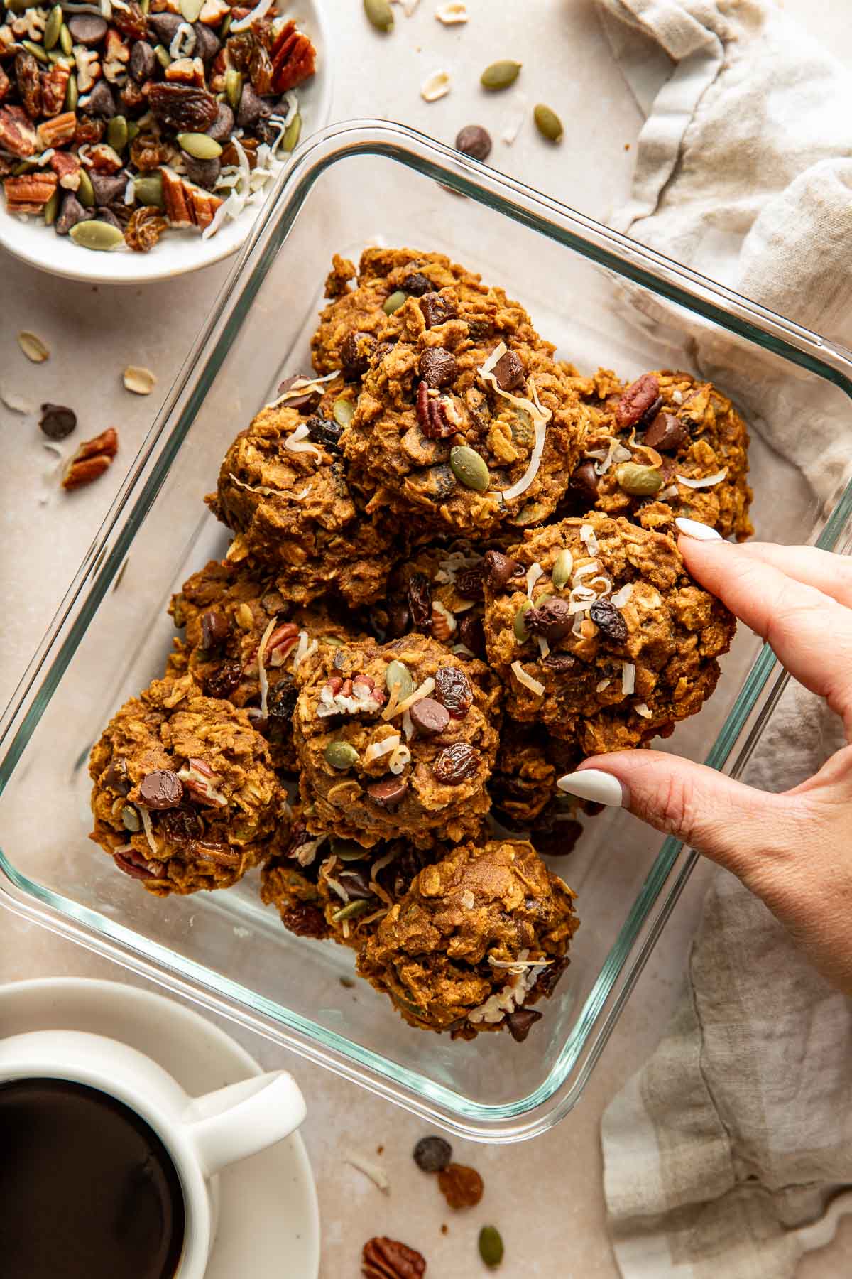 A hand grabbing a pumpkin breakfast cookie from a glass container of cookies.