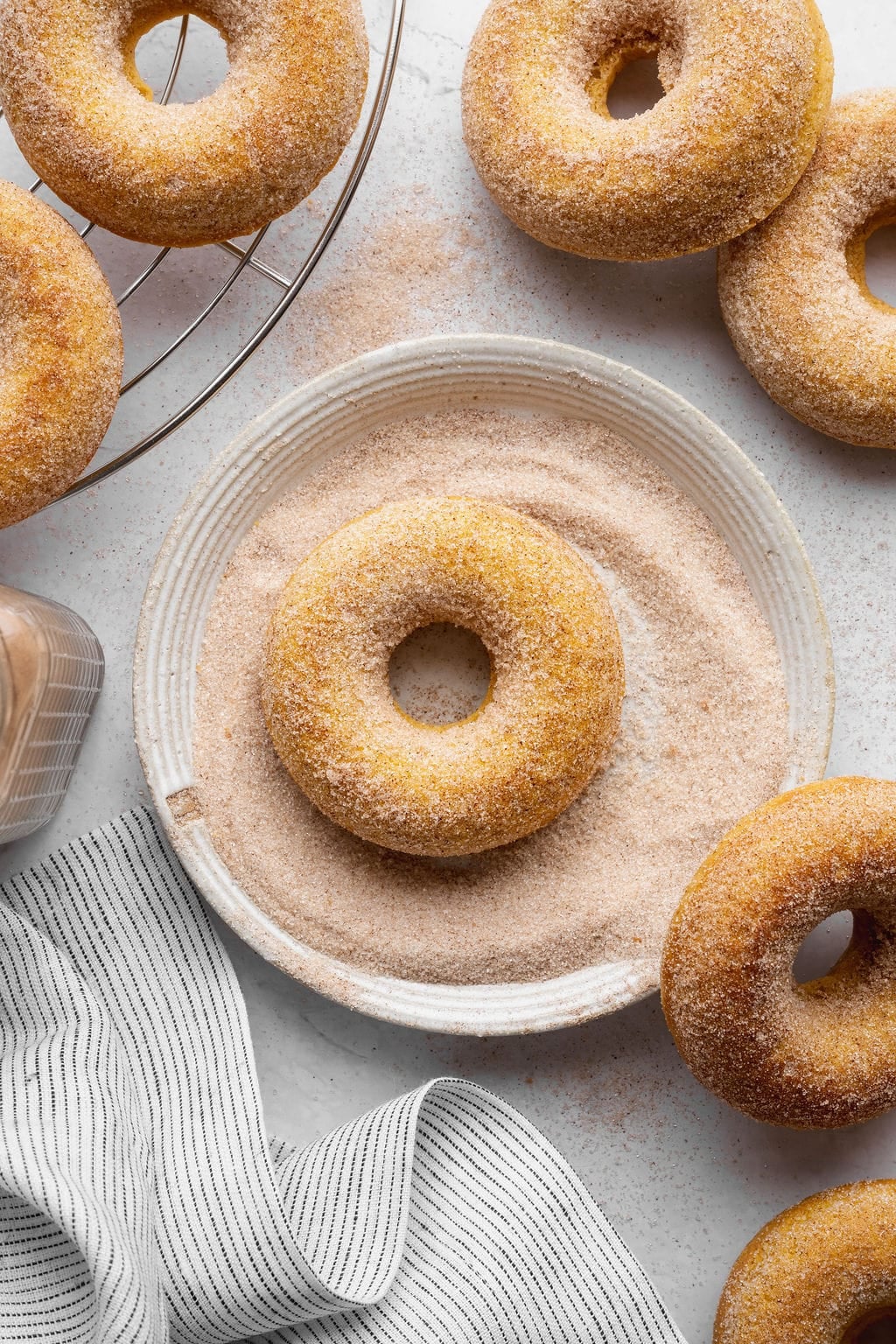 A pumpkin donut in a bowl of cinnamon sugar surrounded by other coated donuts.