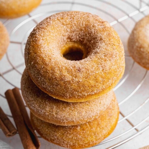 A stack of three baked pumpkin donuts on a wire rack.