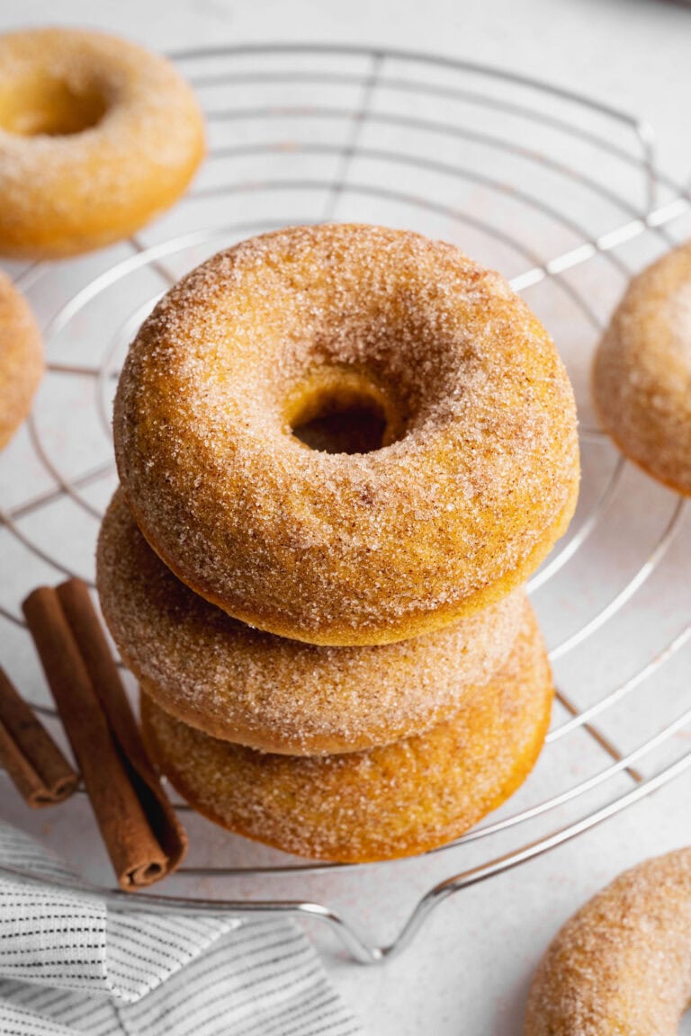 A stack of three baked pumpkin donuts on a wire cooling rack.
