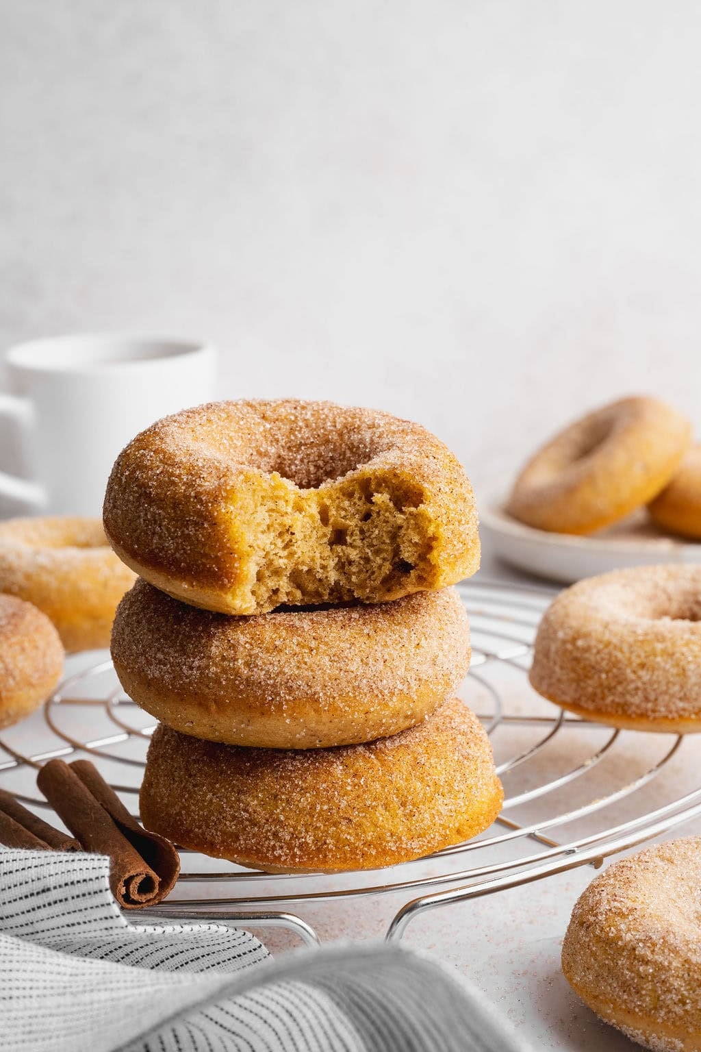 A stack of three baked pumpkin donuts on a wire rack, the top donut missing a bite.