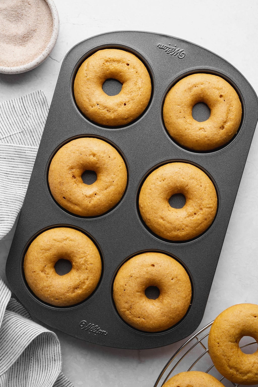 Six baked pumpkin donuts in a donut pan.