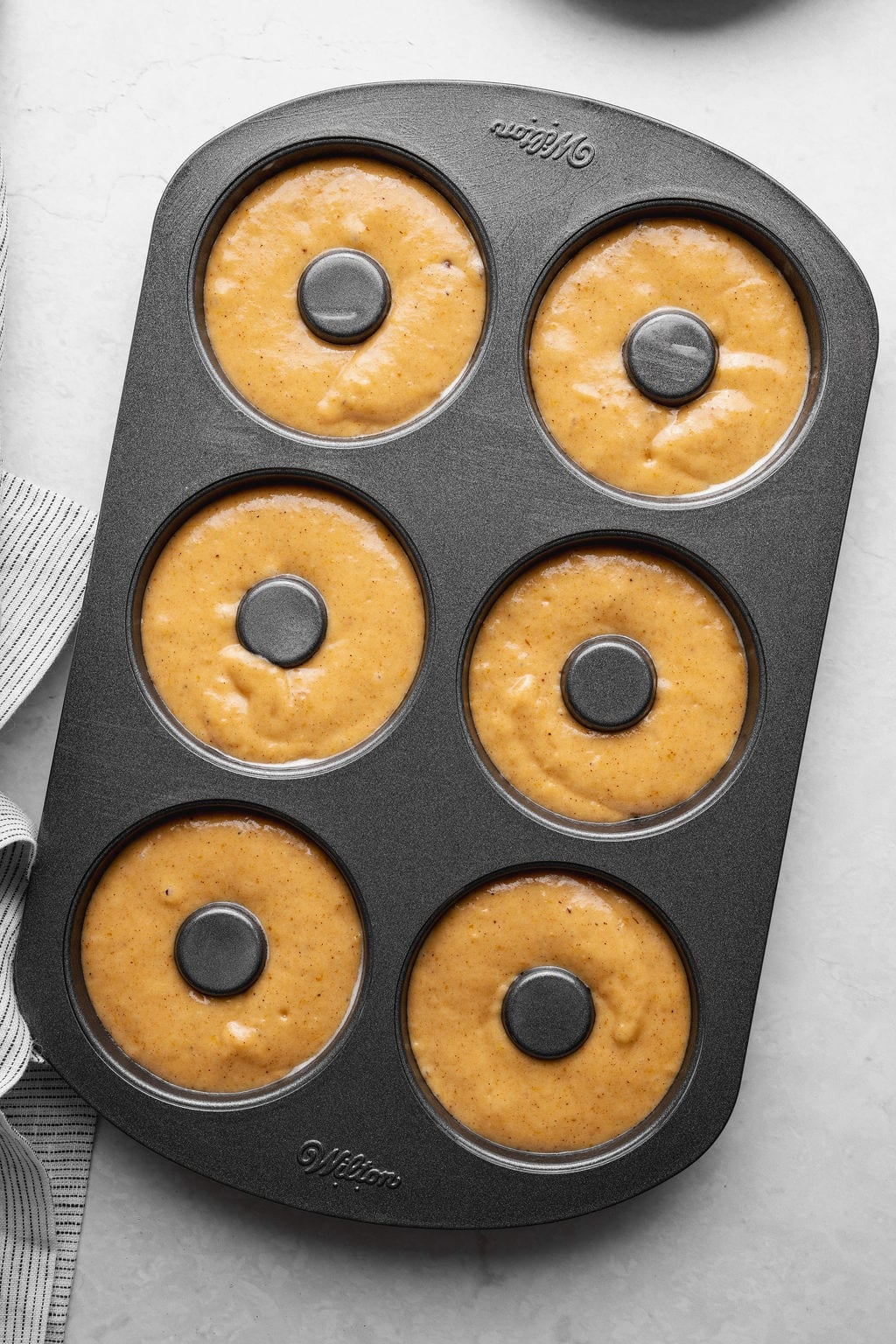 A donut pan filled with raw pumpkin donut batter.