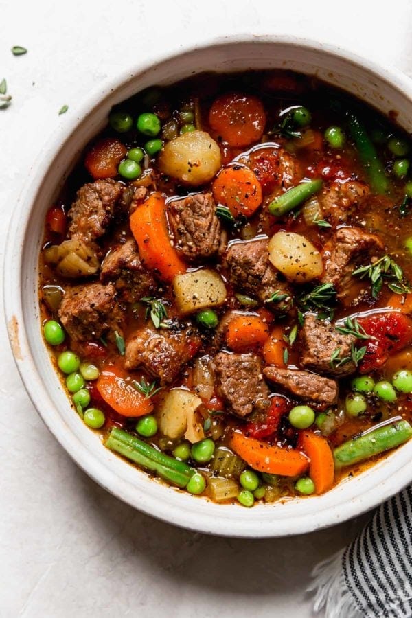 Large chunks of beef, potato, carrot, and peas for vegetable beef soup in a speckled cream bowl ready for serving