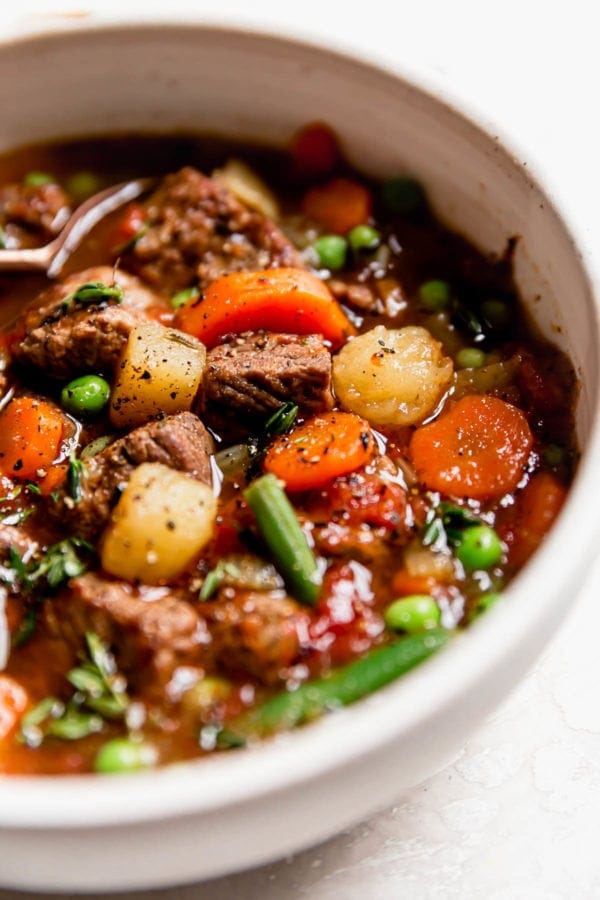 Chunky vegetable beef soup in a cream bowl with cracked pepper on top.