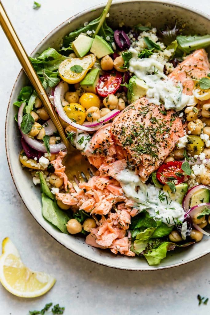 A big salad and grain bowl topped with baked salmon and homemade tzatziki sauce and fresh dill.