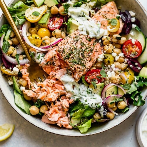 Mediterranean bowl with salmon fillet in a speckled bowl topped with tzatziki sauce