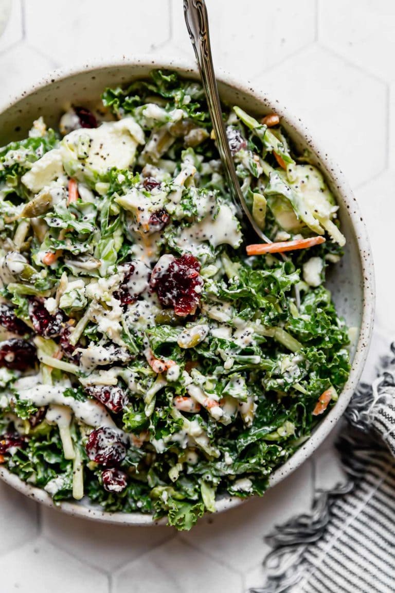 Overhead view of a serving bowl filled with sweet kale salad topped with dried cranberries, pepitas, and goat cheese. 