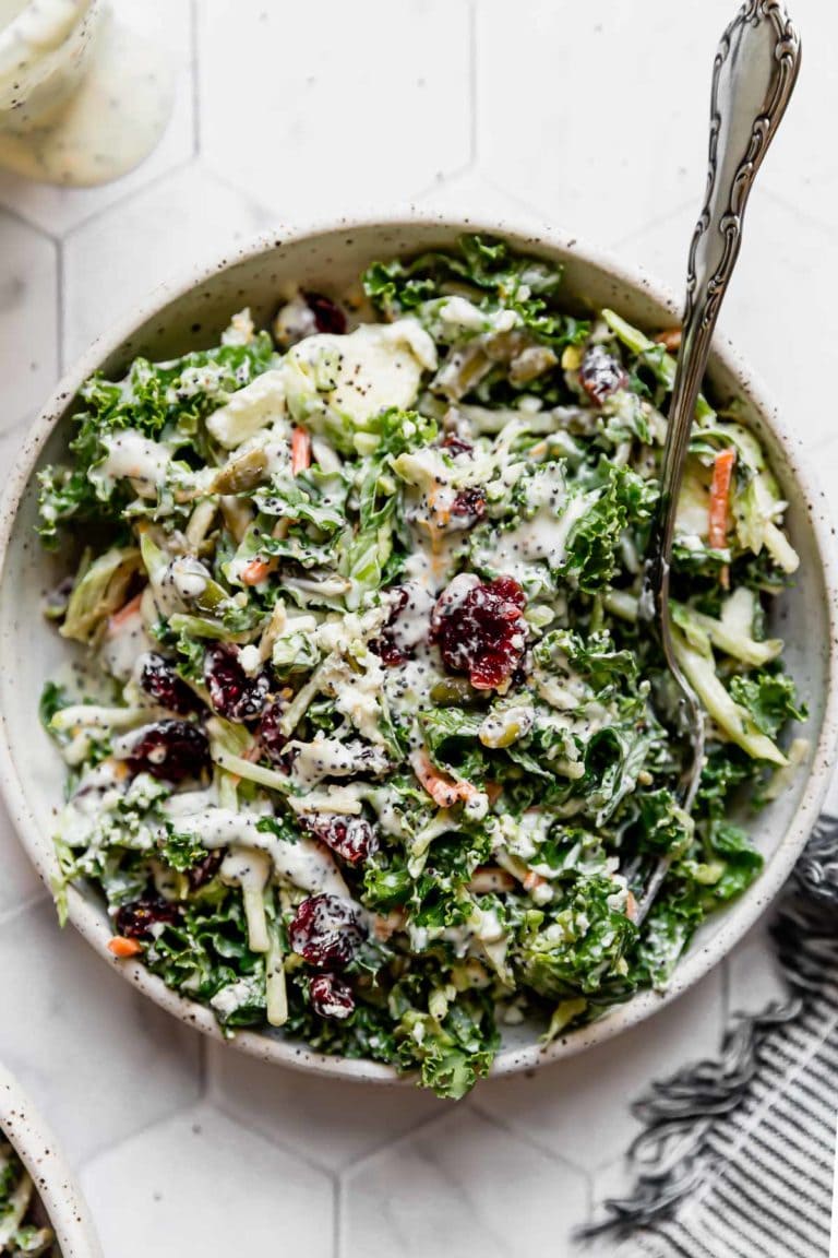Overhead view of a bowl of Kale salad topped with dried cranberries, pepitas, goat cheese, and a poppy seed yogurt dressing. 