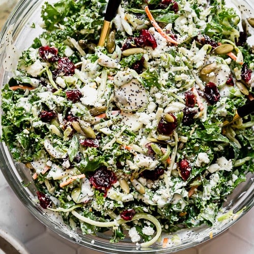 Sweet kale salad tossed in dressing in a clear glass bowl