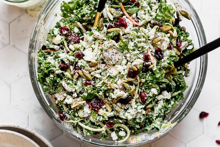 Close up overhead view sweet kale salad in clear glass bowl topped with dressing and dried cranberries.
