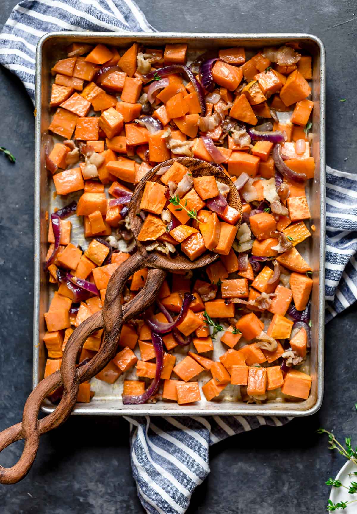 A large wooden spoonful of Roasted Sweet Potatoes with Maple and Bacon resting on a baking sheet full