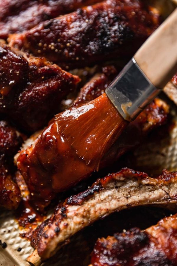 Instant Pot Baby Back Ribs on a baking sheet being mopped with bbq sauce 