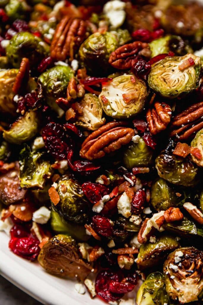 Roasted Brussel Sprouts with Bacon, pecans, cranberries and feta cheese on a white serving platter.