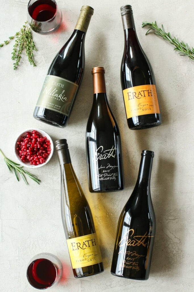 Five bottles of Erath Wine arranged on a white surface surrounded by rosemary sprigs and pomegranate arils.
