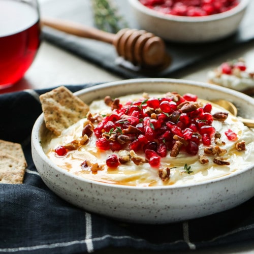 Whipped goat cheese with honey in a speckled bowl topped with pomegranates