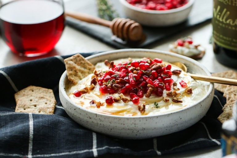 Shallow bowl filled with honey whipped goat cheese topped with pecans and pomegranate arils