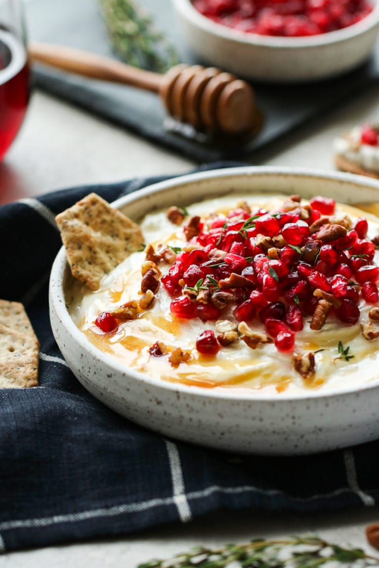 Honey whipped goat cheese in a shallow serving bowl topped with pomegranate seeds and chopped pecans