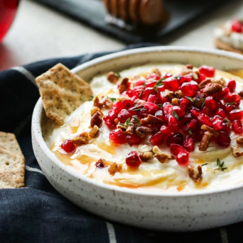 Side view honey whipped goat cheese in shallow bowl topped with pomegranate seeds