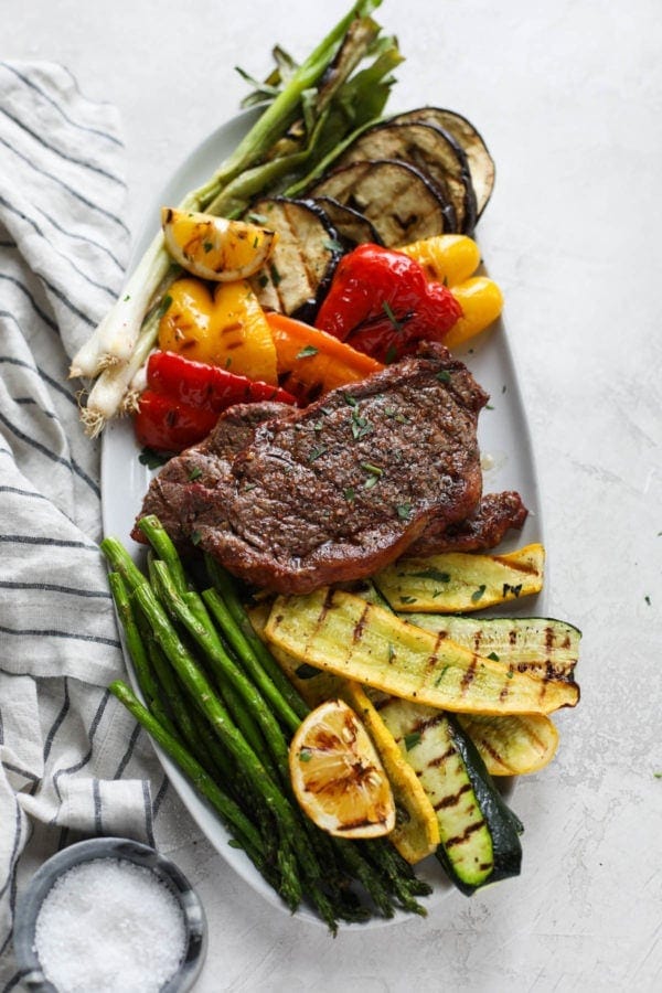 A white platter filled with grilled vegetables and a perfectly grilled steak in the center.