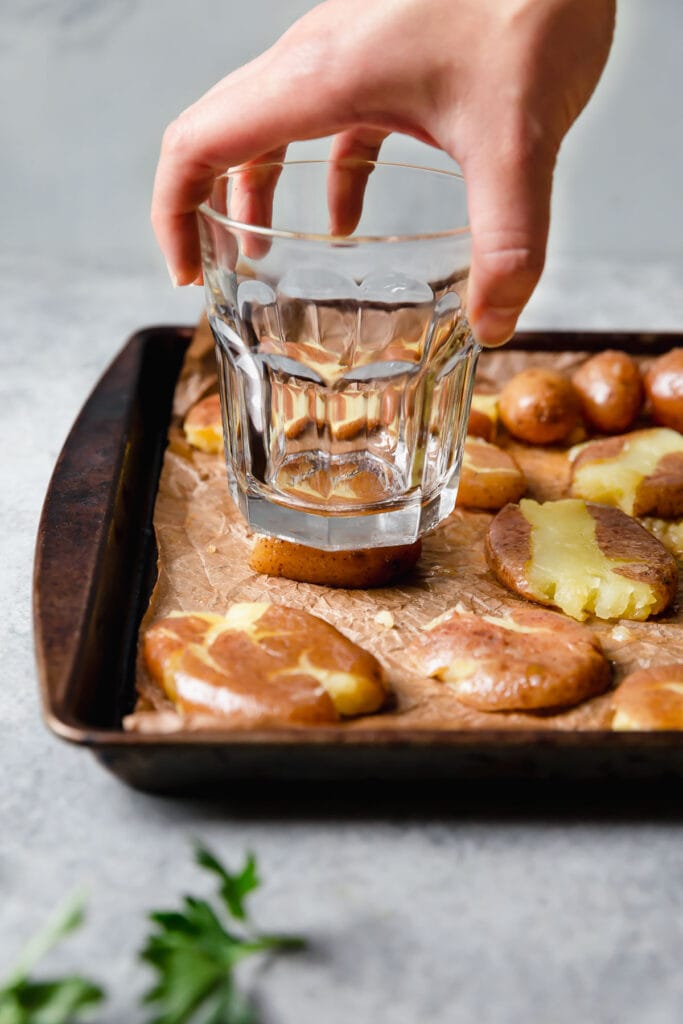 Soft potatoes being 'smashed' by a drinking glass on a baking sheet