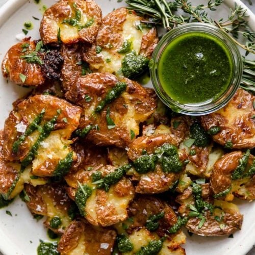 Overhead view of Crispy Smashed Potatoes drizzled with green sauce and topped with flakey salt.