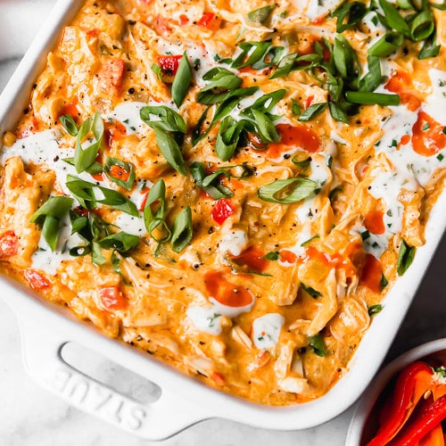 Dairy-free buffalo chicken dip in a white serving dish topped with ranch dressing and scallions.