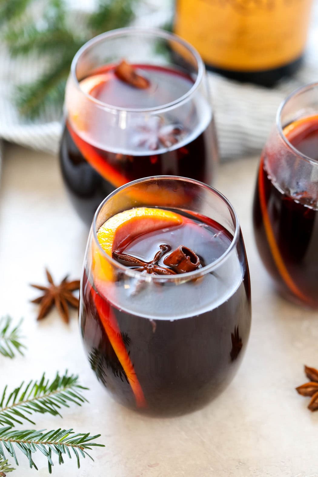 Festive shot of a mulled wine recipe poured into glasses with orange slices and cinnamon sticks.