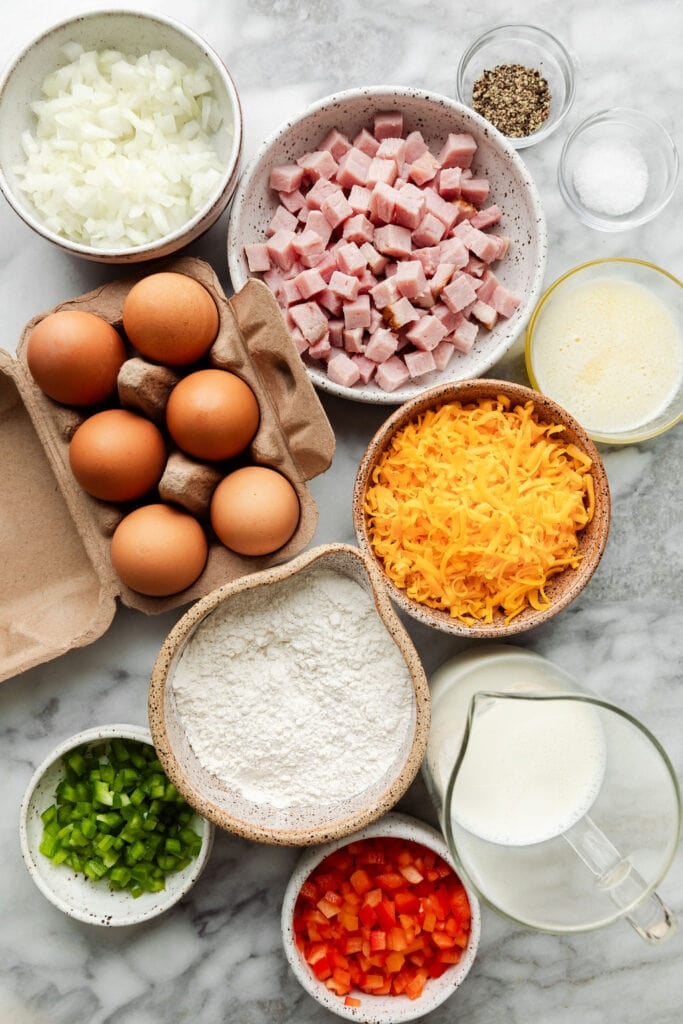 Overhead view all ingredients for ham and cheese breakfast casserole arranged in small bowls and a small egg carton