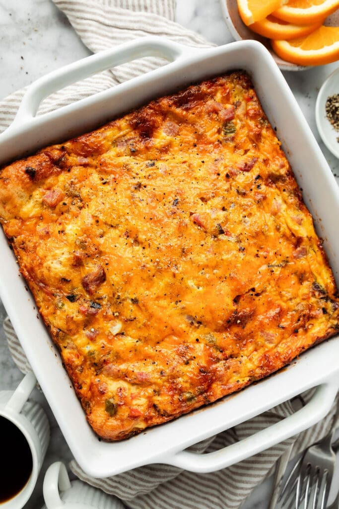 Overhead view baked ham and cheese breakfast casserole topped with melted cheese in white baking dish