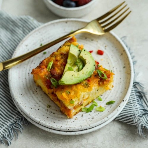 A piece of Western-style breakfast casserole on a speckled plate and topped with sliced avocado.