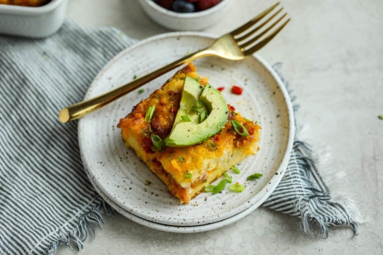 Western-style breakfast casserole served on stone plate, topped with avocado slices.