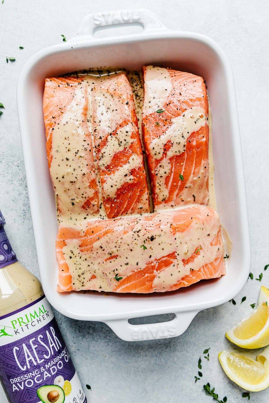 Three salmon fillets in a white baking dish with caesar dressing over the top