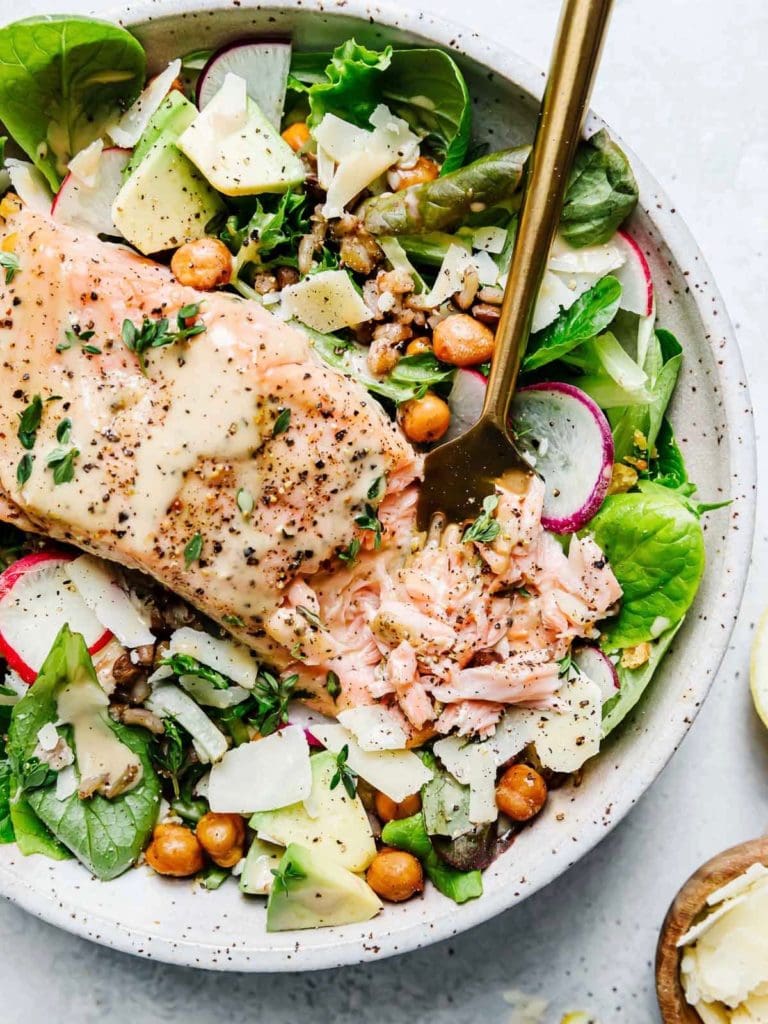 Overhead view of a bowl of Salmon Caesar Salad with shaved parmesan and tender grains. 
