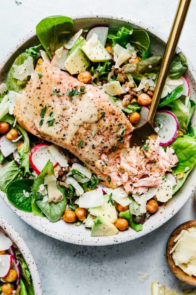 Close up view of a plate of Salmon Caesar Salad Grain bowl topped with fresh herbs. 