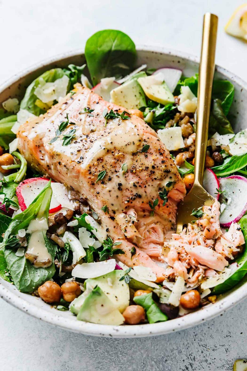 Caesar Salmon Salad Grain Bowl in a speckled stone bowl with greens, avocado, crispy chickpeas and flaky salmon.