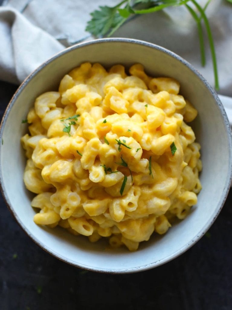 A white bowled filled with dairy-free mac and cheese topped with fresh herbs. 