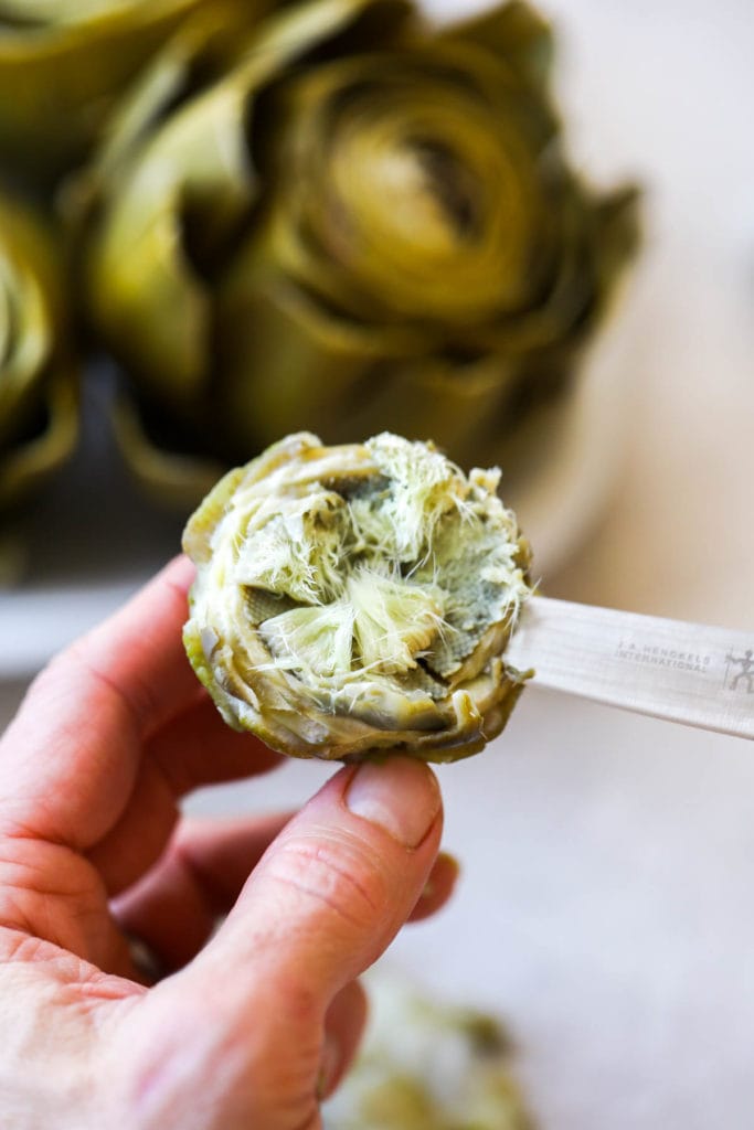 A knife scraping out the meaty edible part of the bottom of the artichoke