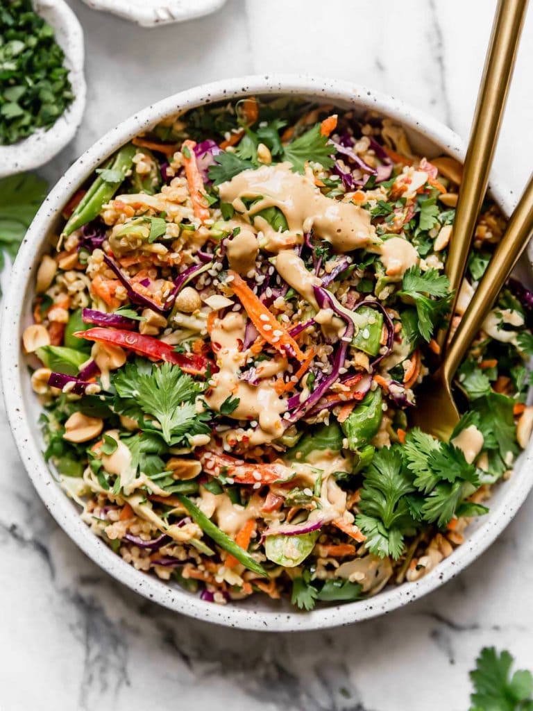 Overhead view of a serving bowl of Thai peanut quinoa salad topped with sesame seeds and fresh cilantro.