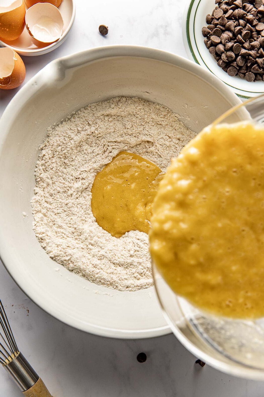 Overhead view of wet ingredients being poured into Banana Muffins dry ingredients in a bowl. 