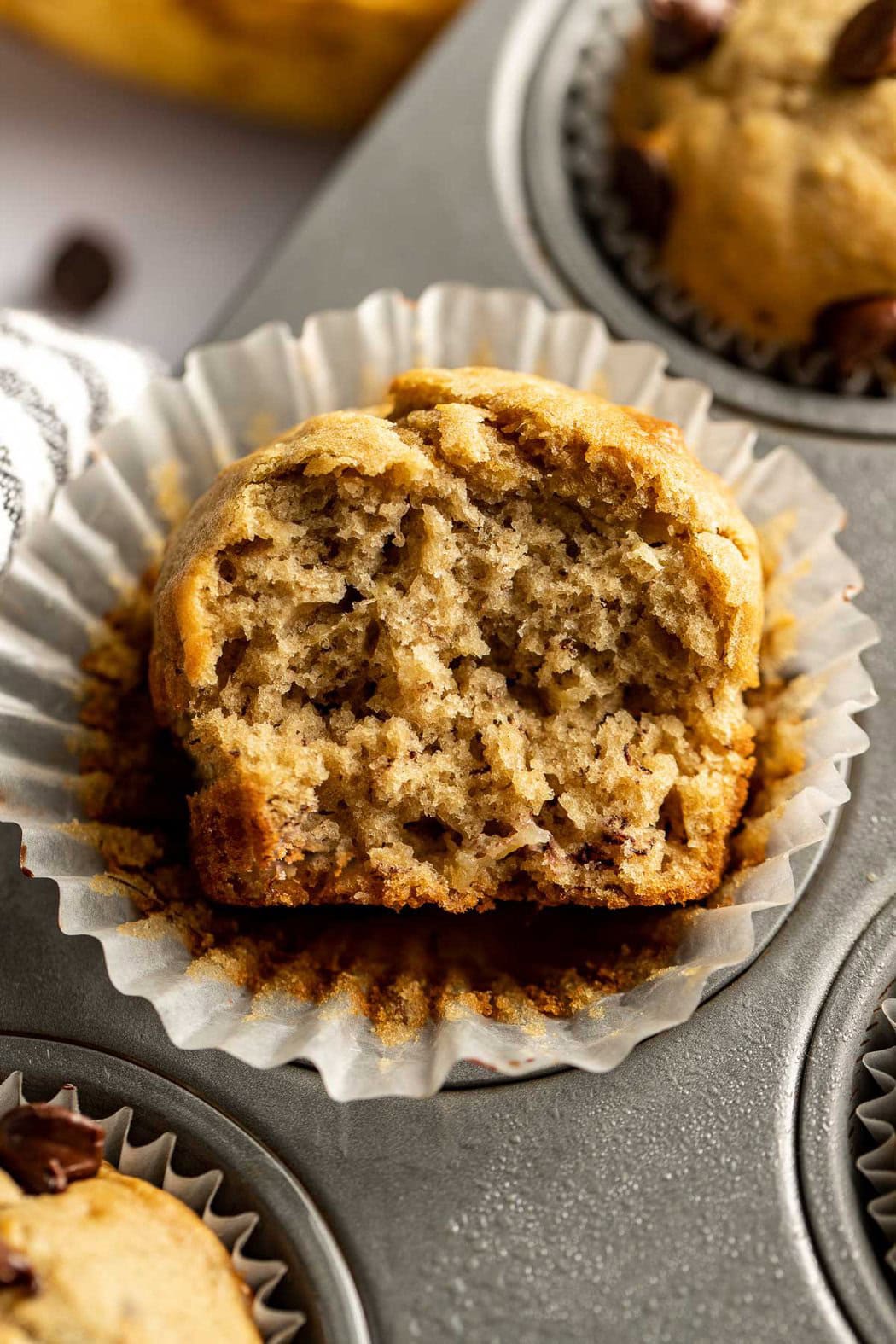 Close up view of a half-eaten Gluten-Free Banana Muffin on a muffin wrapper. 