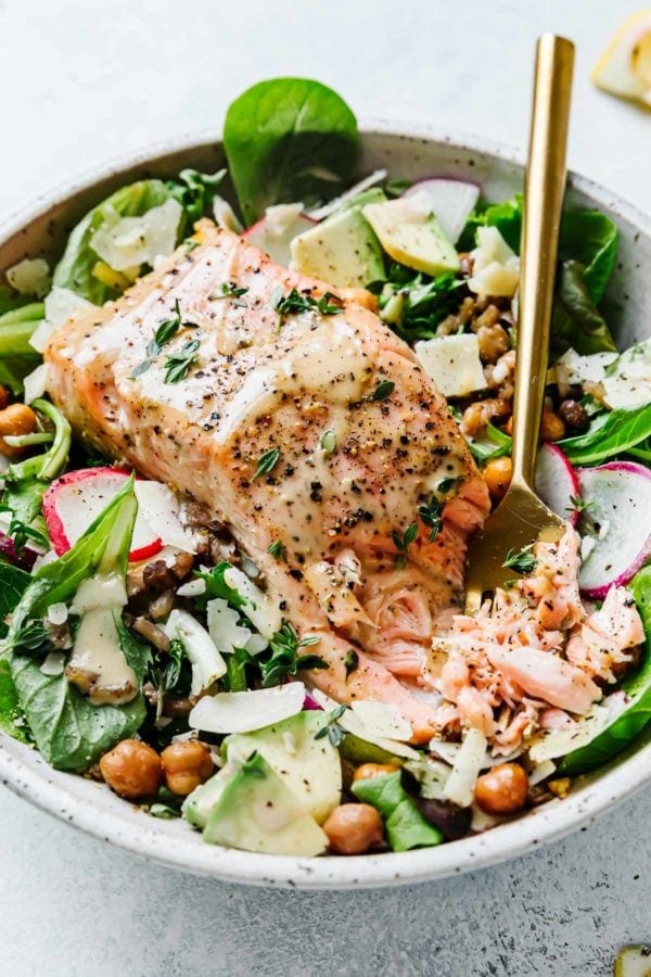 Salmon Caesar Salad served in a bowl of greens topped with caesar dressing, chickpeas, and shaved parmesan
